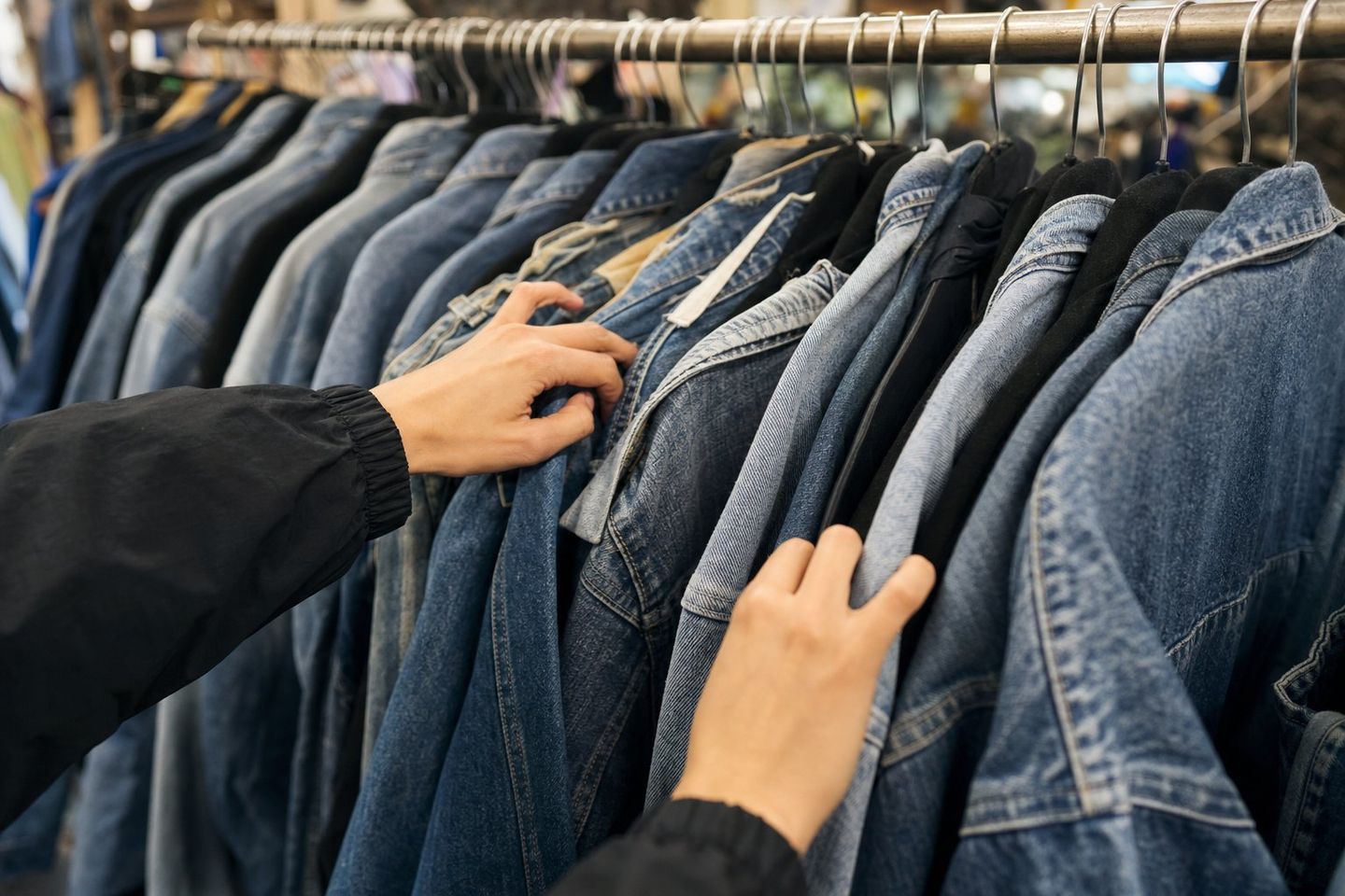 Mains parcourant un rack de jean vintage en friperie