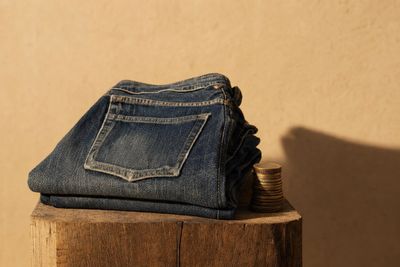 Jean vintage usé plié sur un socle en bois avec une pile de pièces — coût par port