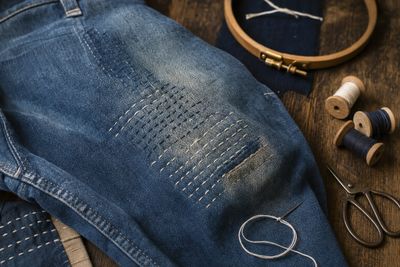 Genou de jean vintage réparé au point sashiko, cercle à broder, bobines et ciseaux — visible mending